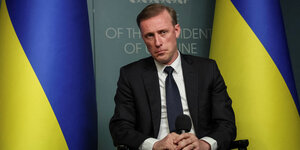 US-Sicherheitsberater Jake Sullivan sitzt zwischen zwei ukrainischen Flaggen und hält ein Mikrofon in der Hand