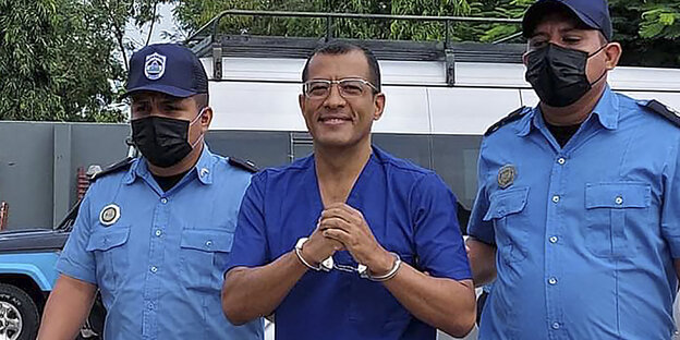 Ein Mann in Handschellen, begleitet von zwei Polizisten.