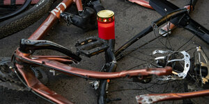 Ein kaputtes Fahrrad und ein Grablicht auf Asphalt.