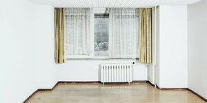 Niedriger Raum, weiß gestrichen mit einem Heizkörper unterm Fenster. am Fenster sind Stores und Gardinen angebracht