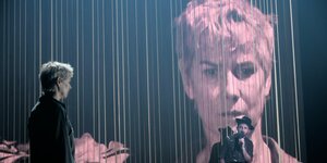 Sylvana Krappatsch steht als Annette auf der Bühne und ist als Projektion groß auf dem Vorhang dahinter zu sehen.