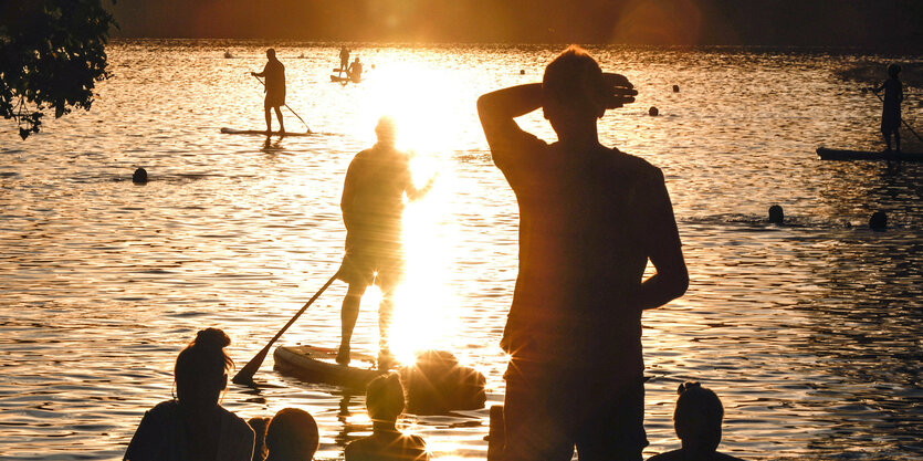 Menschen an einem See im Gegenlicht.