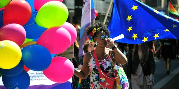 A woman trumpets at a demonstration surrounded by colorful balloons and the EU flag