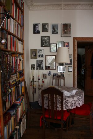 Ein volles Bücherregal, daneben ein Tisch und eine Stehlampe, an den Wänden zahllose gerahmte Bilder Ein volles Bücherregal, daneben ein Tisch und eine Stehlampe, an den Wänden zahllose gerahmte Bilder