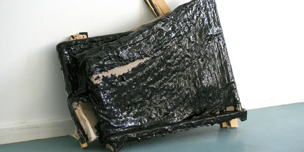 Ausstellungsansicht im Künstlerbund Berlin in die Ausstellung "Tasty Painting". Die Arbeit „Ghost II“ von Peter Pumpler, ein dekonstruiertes abstraktes Gemälde, liegt am Boden an die Wand gelehnt. Über einem durchgebrochenen Keilrahmen staucht sich Leinwand, die mit schwarz glänzendem Bitumen übergossen ist.
