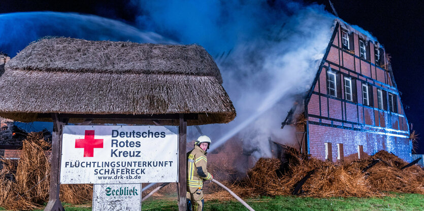 Ein Feuerwehrmann vor einem brennenden Haus.