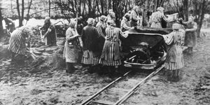 Frauen in Häftlingskleidung schaufeln Erde auf einen Lore auf Schienen