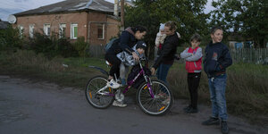 Zwei ukrainische Frauen mit vier Kindern und einem Kinderfahrrad auf einer Dorfstraße