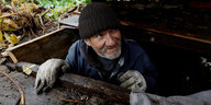 Ein älterer Mann mit schwarzer Mütze klettert aus einem Kellerloch