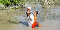 Ein Mann trägt ein Mädchen durchs Überschwemmungsgebiet