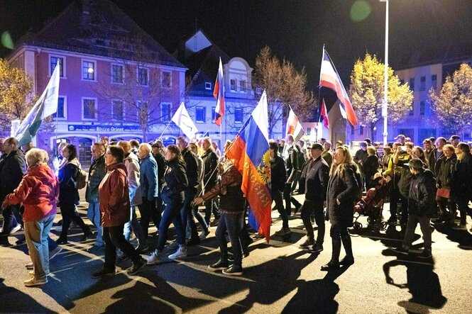 Teilnehmer einer Demonstration gehen mit verschieden Flaggen, darunter einer russischen Nationalflagge, über den Kornmarkt.