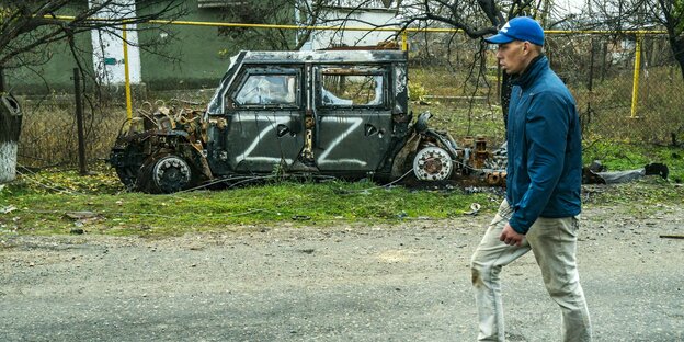 Ein Passant geht an einem zerstörten Militärfahrzeug vorbei. Darauf ist zwei Mal in weißer Farbe der Buchstabe "Z" gesprüht.