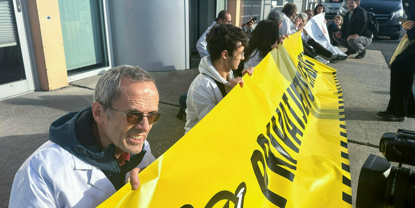 Mehrere Personen mit weißen Kitteln sitzen hinter einem Banner