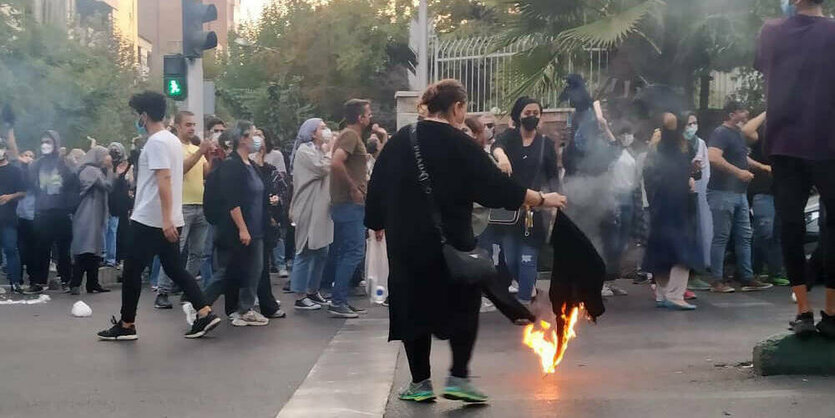 Eine Frau verbrennt ihr Kopftuch bei einer Demonstration.