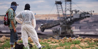 Aktivisten stehen am Loch des Braunkohletagebaus, im Hintergrund steht ein großer Abraumbagger