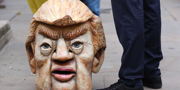 A protester stands next to a replica of President Trump's head in Parliament Square