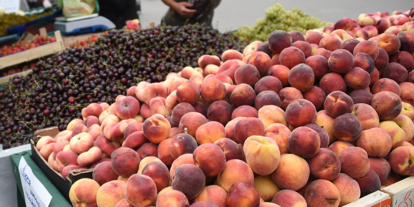 Ein Marktstand mit einem großen Berg appetitlicher Pfirsische, dahinter liegen Kirschen