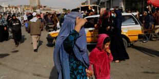 Personen laufen in Kabul über eine Straße, eine Frau mit Kind ist verschleiert