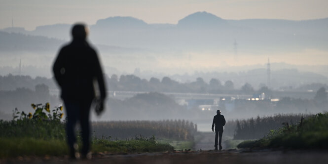 Spaziergänger gehen auf einem Feldweg, im Hintergrund ist der Rand der Schwäbischen Alb zu sehen.