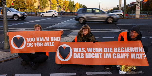 Straßenblockade mit orangem Transparent, 3 Aktivisten sitzend