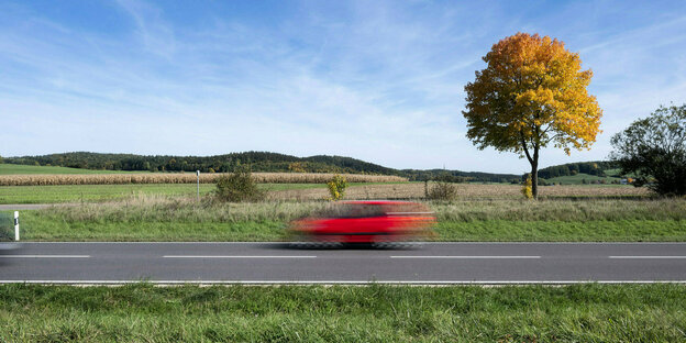 Ein kleines rotes Auto braust durch eine herbstliche Landschaft