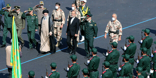 Soldiers in green uniforms stand in line - Ayatollah Khameini, accompanied by commanders in uniform, walks past the soldiers