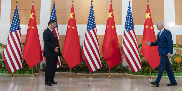 Biden approaches Xi Jinping with his hand outstretched, behind them are Chinese and American flags