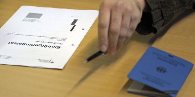 A man's hand holds a pen next to a naturalization test