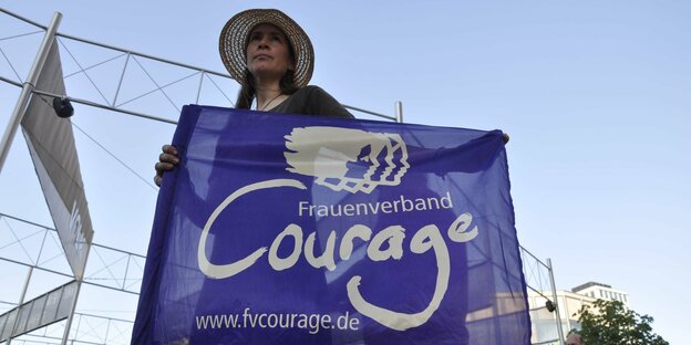 Eine Frau mit Sonnenhut hält eine Fahne des Courage Frauenverbands