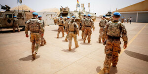 Soldaten gehen in einer Gruppe, sie tragen blauer Kopfbedeckung, von hinten aufgenommen