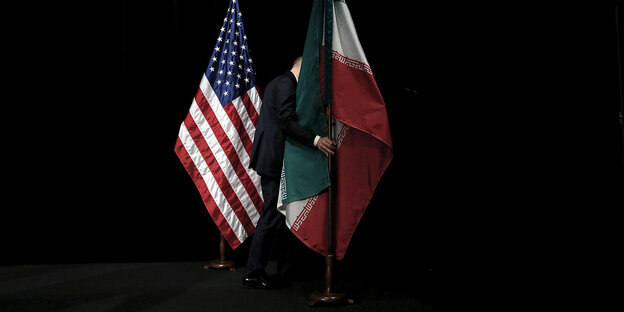 A person between a flag of the USA and a flag of Iran