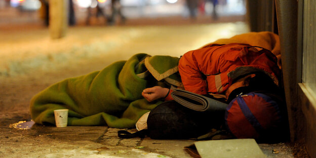 ein Obdachloser liegt in seinem Schlafsack auf einem Gehweg