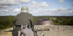 Ein Mann, der als ein Soldat aus dem Ersten Weltkrieg verkleidet ist, sitzt auf einer Mauer und schaut in die Landschaft.