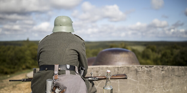 Ein Mann, der als ein Soldat aus dem Ersten Weltkrieg verkleidet ist, sitzt auf einer Mauer und schaut in die Landschaft.