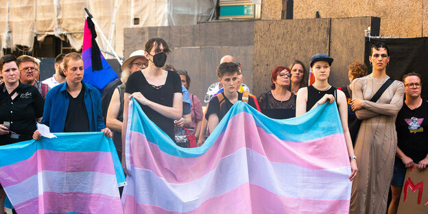 Personen stehen hinter einem Transparent in Trans-Farben