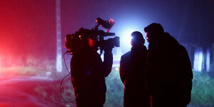 Drei Journalisten, einer davon mit Kamera, im Zwielicht der Nacht des Raketeneinschlags in Przewodow, nahe der Grenze mit der Ukraine