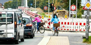 Zwei Fahrradfahrerinnen versuchen eine Straße zu überqueren, Baustelle, Autos und Schilder behindern die Weiterfahrt