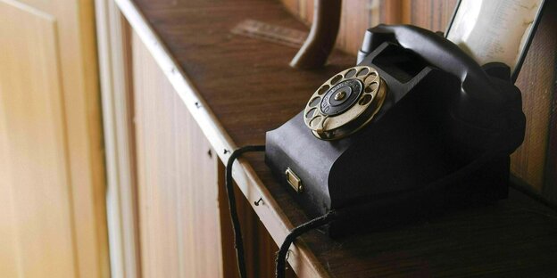Ein schwarzes Telefon mit Wählscheibe steht auf einer Ablage aus Holz