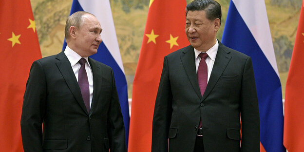 Putin and Xi stand in front of their countries' flags.