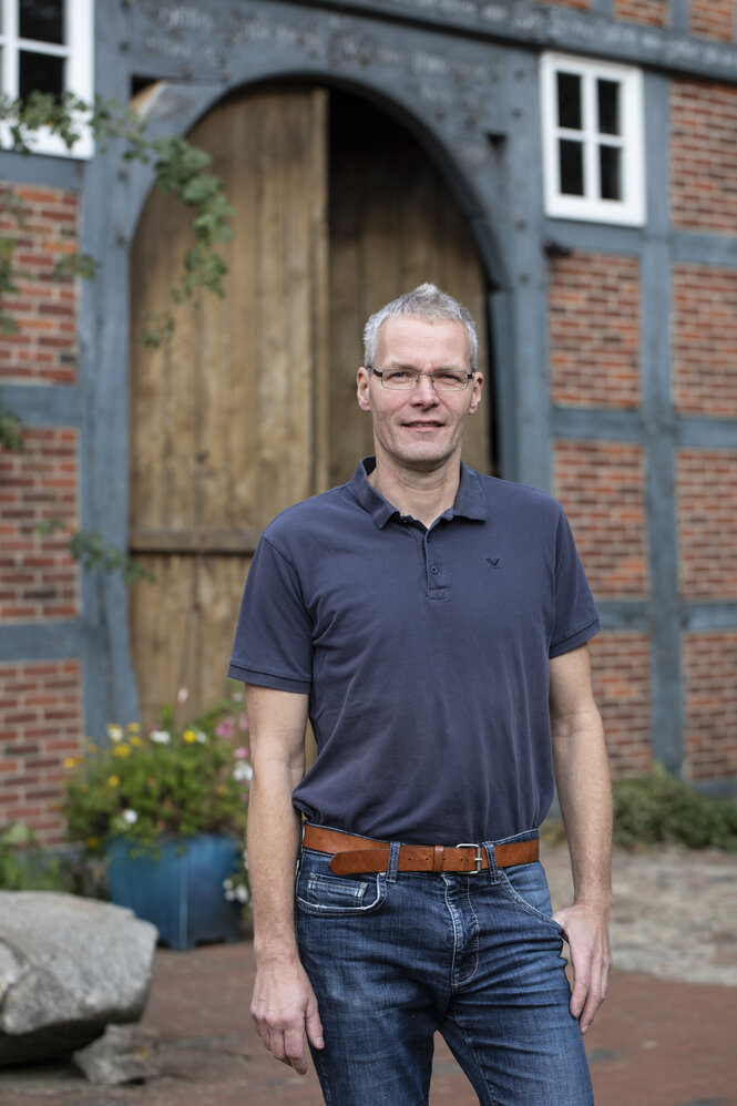 Ein Mann im kurzärmeligen Hemd steht vor einem Backsteinhaus