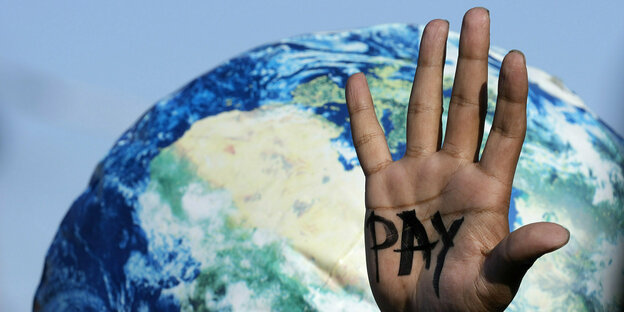 Eine Hand, in deren Innenflächen das Wort "Pay" aufgemalt wurde, ist vor einer Weltkugel zu sehen