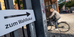 Ein Mensch auf einem Rad fährt an einem Schild mit der Aufschrift Wahllokal vorbei