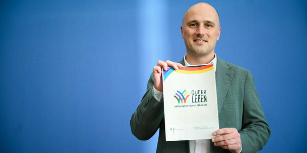 Sven Lehmann hält die Broschüre " Queer Leben" in die Kamera
