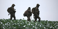 Drei Soldaten in Uniform mit Rucksäcken gehen über eine Feld