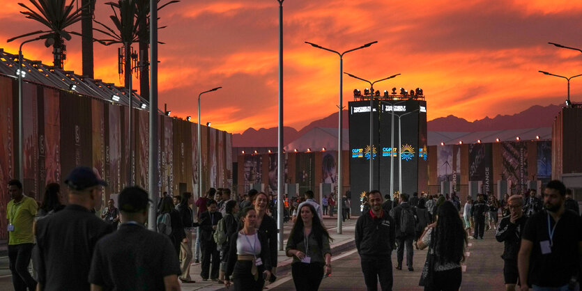 Menschen laufen im orangefarbenen Dämmerlicht über das Außengelände der COP 27.