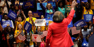 eine Frau in rotem Jacket steht vor einer Anhängern mit Schildern auf denen "Vote, Union Strong und Vote Florida" zu lesen ist