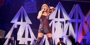 Taylor Swift steht in kurzem Kleid und Overknee-Stiefeln auf der Bühne und singt