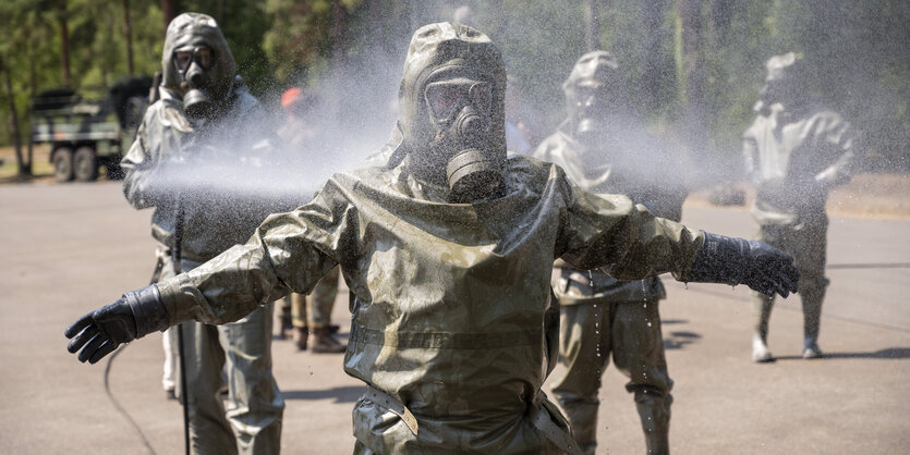 Soldaten in Schutzanzügen spritzen sich ab