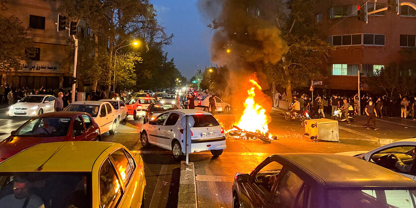 Ein brennendes Motorraad liegt auf einer befahrenen Kreuzung