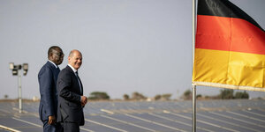 Der Präsident von Senegal Macky Sall und Scholz stehen auf dem Dach einer Photovoltaikanlage, davor weht die deutsche Fahne